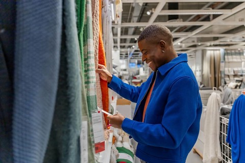 A young African man in a blue jacket examines colorful fabric swatches in a modern retail store. He