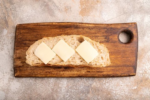 Slice of homemade bread with butter on cutting board on brown concrete background, close up, top