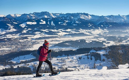 Nice and active senior woman snowshoeing in in the snow covered Allgaue alps above the valley of