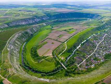 A vast, green landscape with a river flowing through fields and hills, viewed from the air, aerial