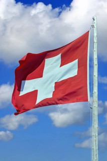Swiss flag waving against blue sky and cumulus clouds, Swiss national flag