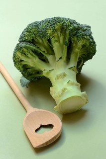 Broccoli with cooking spoon on green background