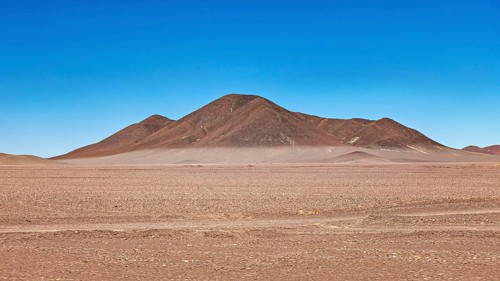 Lonely mountain in the middle of a vast, dry desert landscape under blue skies, The Moon Valley in