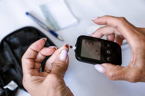 Close-up of female hands inserting a test strip into a blood glucose meter before diabetes testing.