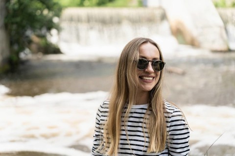 Smiling long-haired woman in sunglasses near the river opposite the dam, A woman wearing sunglasses