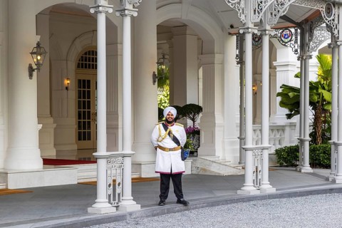 Turbaned Sikh doorman standing at the colonnaded entrance of Raffles Hotel, Singapore