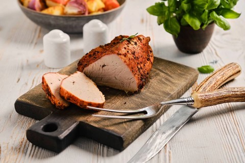 Oven roasted turkey breast is placed on wooden cutting board with slices cut. Knife and fork lie
