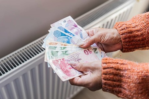 Woman holding Turkish lira banknotes near home radiator during winter heating season. Concept of