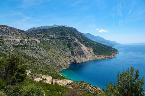 Wide coastal landscape with mountains and blue sea under clear sky, peaceful atmosphere, Pisak,