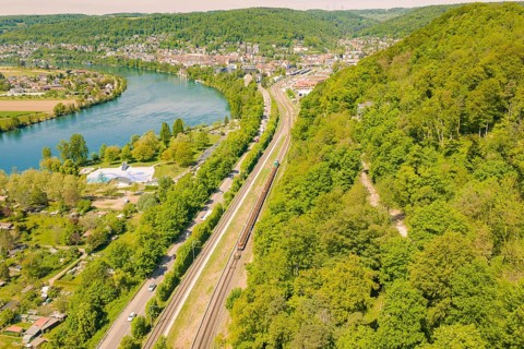 Railway line along a river in a wooded and urban environment in spring, construction site by
