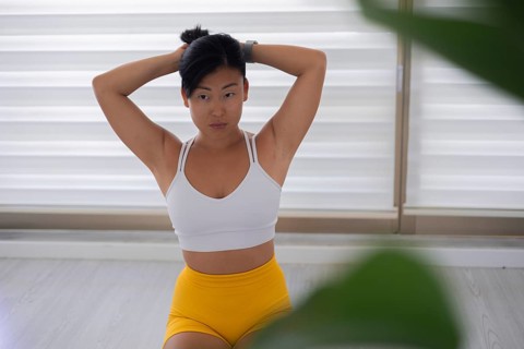 Woman in workout clothing stretching with her arms raised indoors