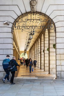 Pedestrians pass beneath the stone arcade and lanterns of The Ritz Hotel on Piccadilly, London,