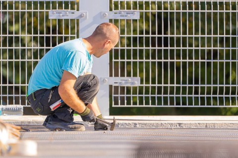 Construction worker kneels and works with a hammer in front of a safety fence in sunny weather,