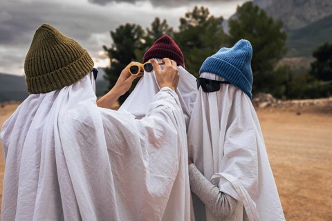 Three young people dressed as ghosts in white sheets, wearing colorful beanies and sunglasses,