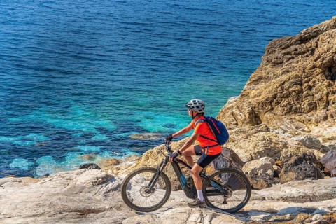 Nice woman riding her electric mountain bike at the coastline of mediterranean sea on the Island of
