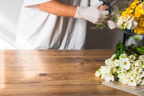 A florist carefully trims the stems of white and yellow flowers in transparent wrapping. Closeup of