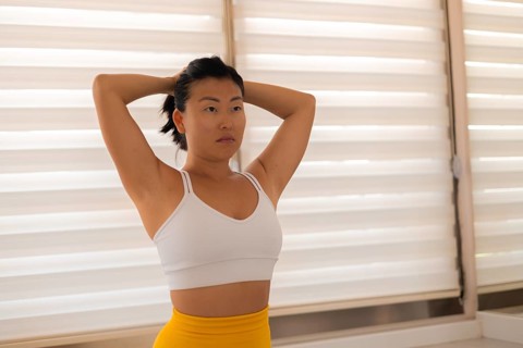 Woman standing with hands on head looking thoughtfully at blinds