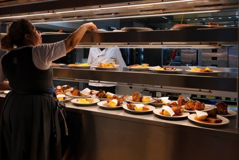 Interior view, from the kitchen, cook, orders placed on counter, dishes such as pork knuckle with