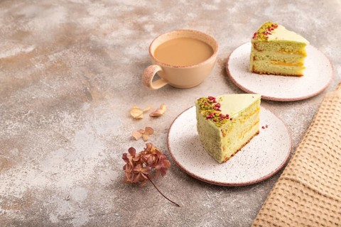 Pistachio green cake with cup of coffee on brown concrete background with beige textile, copy