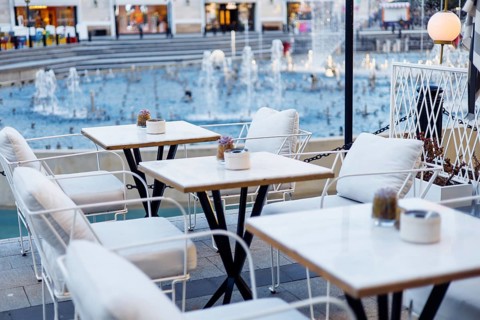 Cozy tables and chairs set near a beautiful fountain in a lively urban environment. The soft glow