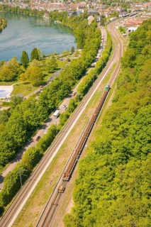 Aerial view of a railway line along a forest next to a river in an urban environment, construction