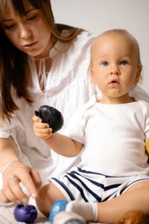 Baby watching intently while mother points out a toy