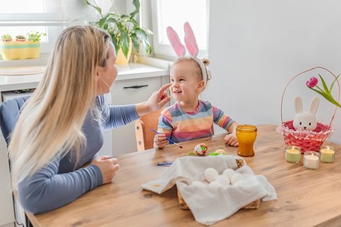 Mother and toddler girl daughter painting Easter eggs at home in modern kitchen. family tradition,