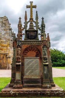 A Gothic Revival memorial cross and carved monument stand in the grounds of 15th century Rosslyn