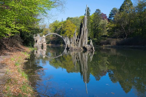 Reflection of a stone landscape structure in the calm water of a forest, Rakotz Bridge, Devil's