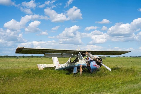 An abandoned, damaged aircraft is lying in a field under a blue sky with clouds, PZL-104 Wilga