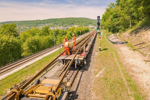 Worker on a rail maintenance platform in a rural area with forest and sky, Leonhard Weiss