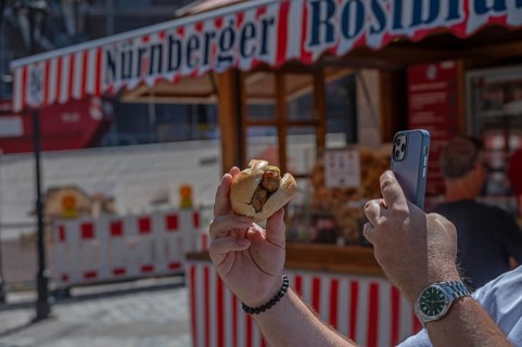 Tourist photographs Nuremberg bratwurst in a roll with his mobile phone, Nuremberg, Middle