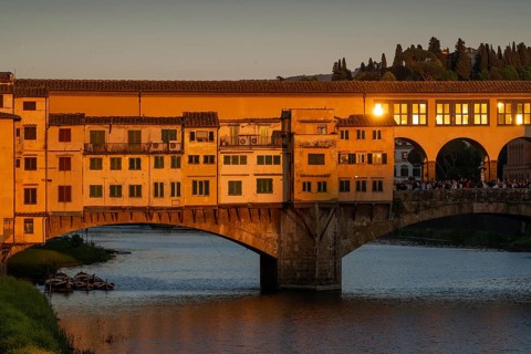 Warm evening light falls on the historic Ponte Vecchio segmental arch bridge across the Arno River