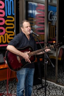 A middle-aged Caucasian man with short brown hair sings and plays an acoustic guitar in a vibrant