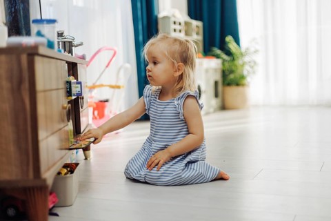 Child girl interacts with a storage unit filled with toys in a sunny indoor space
