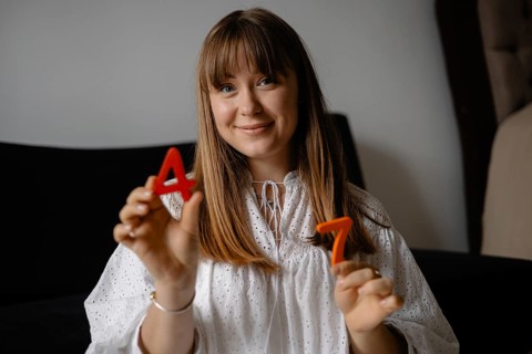 A woman indoors holds red numbers 4 and 7, smiling casually