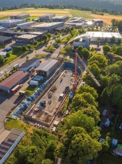 Aerial view of a construction site with crane and buildings surrounded by forests and roads in