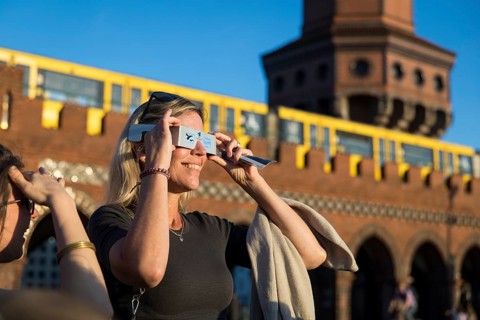 People wearing goggles watch the solar eclipse just in front of sunset on the Oberbaum Bridge in