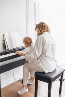 A woman and child sit at a piano from the backside, in a peaceful and bright room