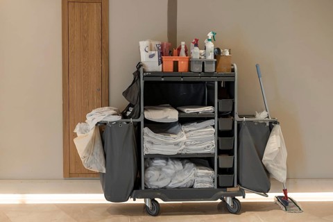 A cleaning cart filled with supplies, including towels, cleaning products, and a mop. The cart is