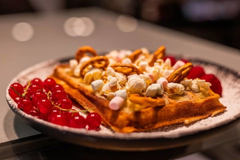 A delicious waffle topped with popcorn, marshmallows, and nuts, served with fresh red berries on a