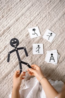 A person holding a stick figure toy with illustrated cards on a textured floor