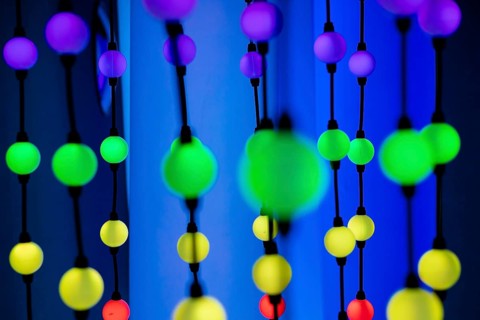 Colorful decorative beads in various sizes and colors, hanging against a vibrant background. The
