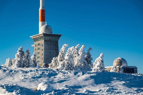 View over snow-covered spruce trees of the icy Brocken Hotel and the telecommunications tower on