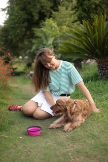 Woman sitting on a grassy path petting her dog, with tropical plants around them