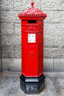 A hexagonal red pillar post box with an ornate crown finial and royal cypher stands against a