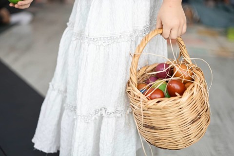 A young Caucasian woman in a white dress holds a woven basket filled with colorful apples. The