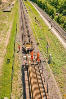 Tracks with working railway workers in summer, surrounded by green landscape, construction site by