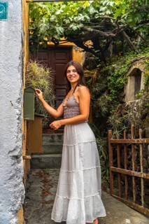 Young woman smiling while opening a green mailbox in a rustic village setting with lush hanging
