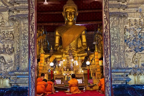 Buddhist monks and novices sit in front of a large Buddha statue in Wat May Souvannapoumaram, Luang